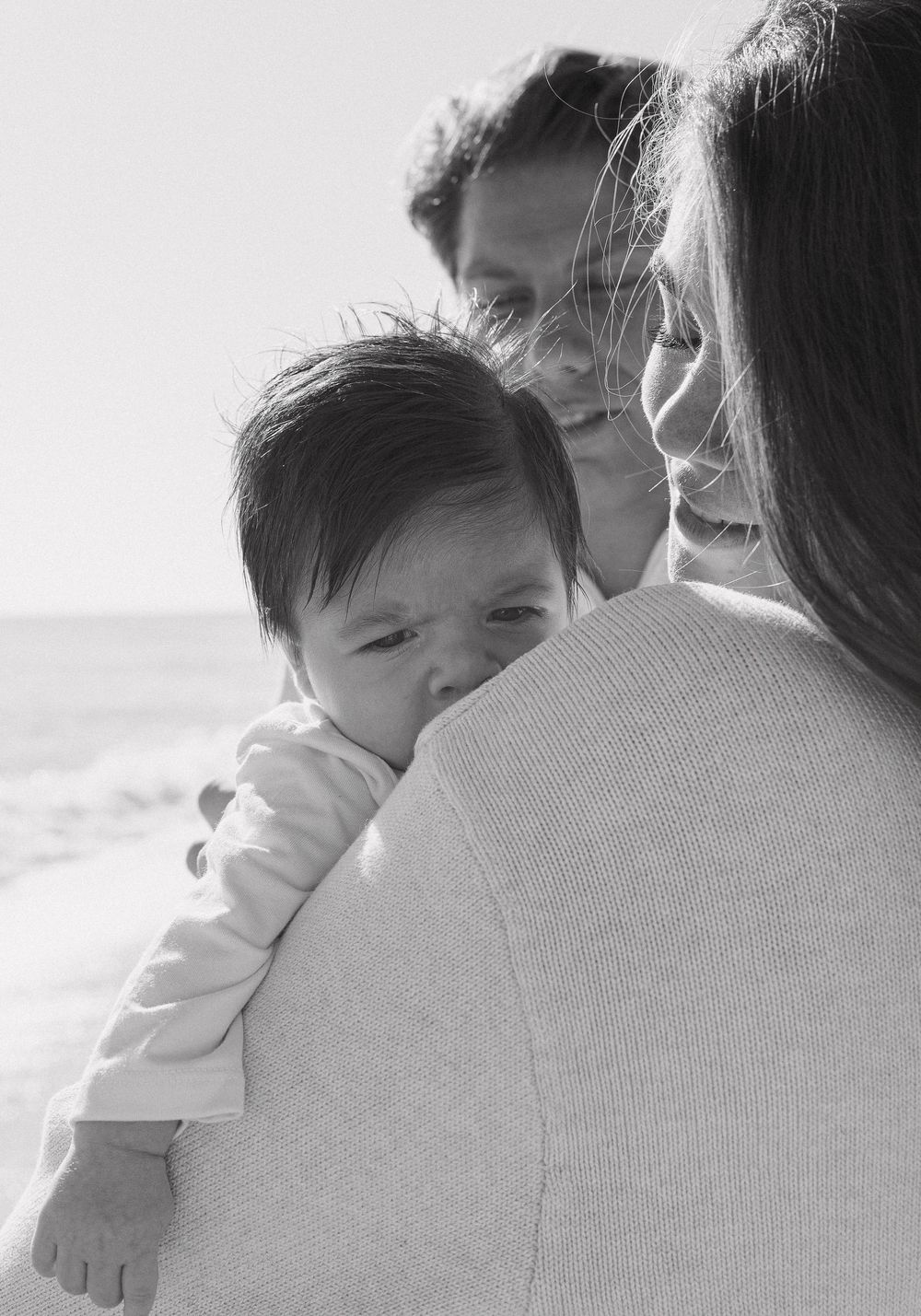 Tender family moment captured in black and white photography at the beach.