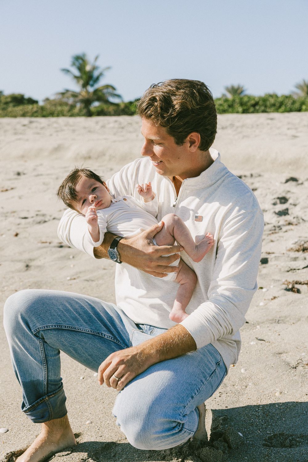 Candid beach moments captured in a series of relaxed poses on sandy shores wearing casual white and denim.