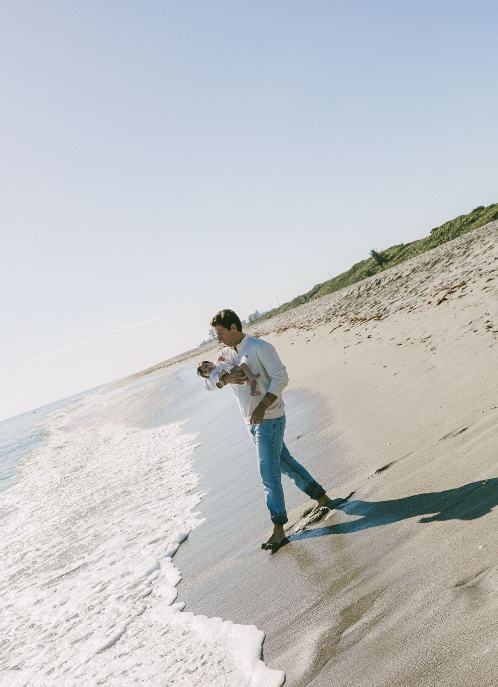 People walking and playing on a sandy beach slope near ocean waves.