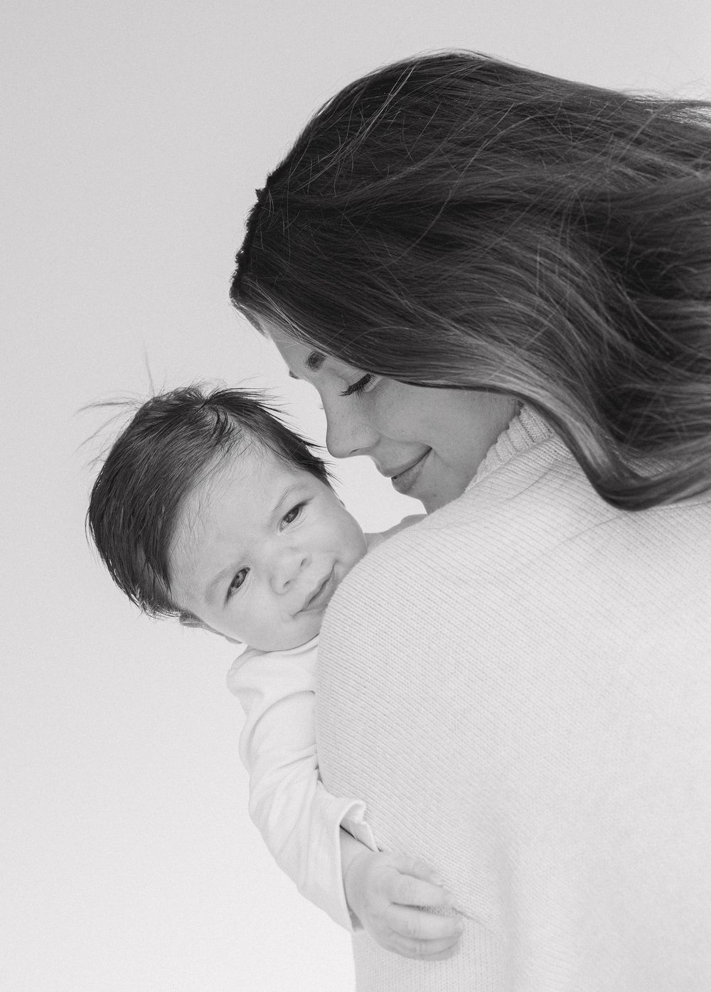 A tender black and white portrait of a parent and baby sharing an intimate moment.