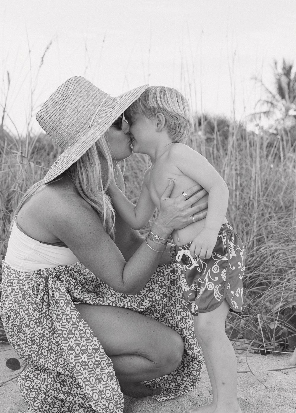 Black and white sequence showing tender moments between parent and child on a sandy beach.