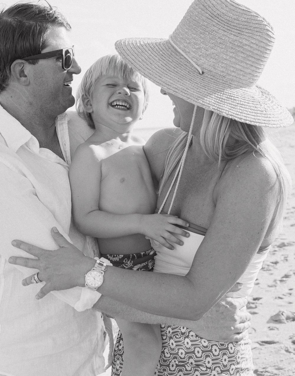 A loving family moment captured in black and white as they embrace and play together on a sunny beach.