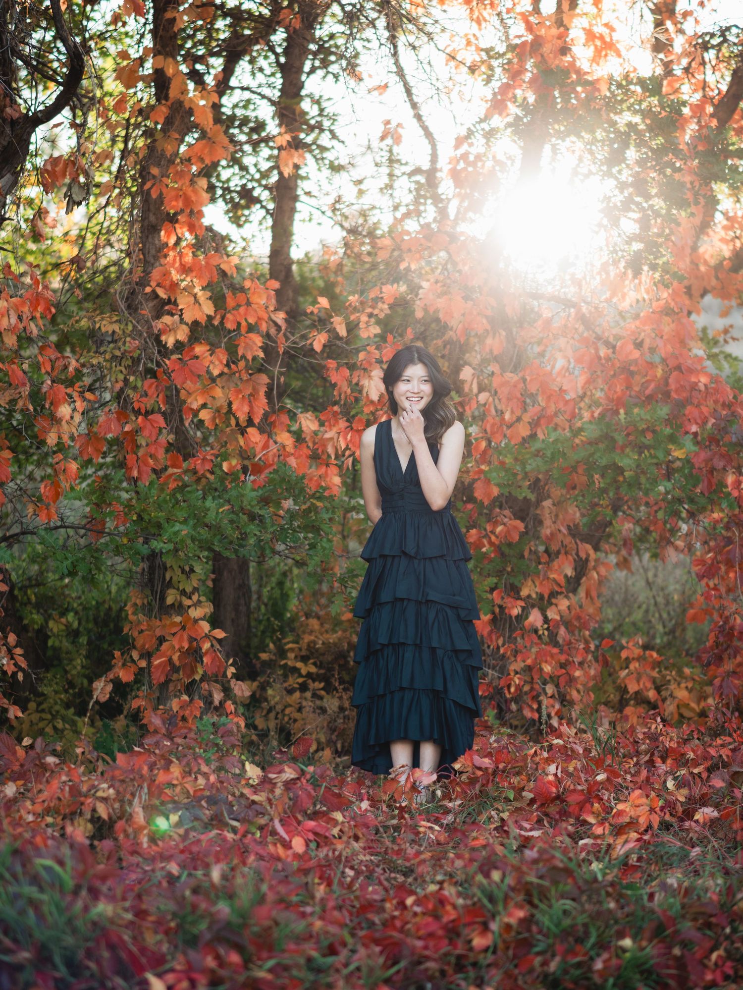 A figure stands among vibrant red autumn foliage and trees during golden hour sunset creating a dreamy atmosphere.