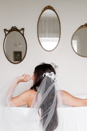 A minimalist white wall features multiple vintage oval mirrors above a figure wearing a delicate bridal veil.