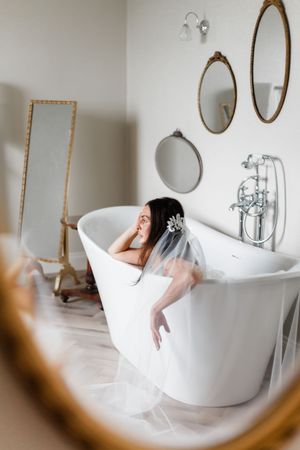 A vintage-style bathroom with a freestanding tub, oval mirrors on the wall, and flowing white tulle fabric.