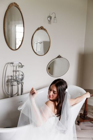 A white freestanding bathtub in an elegant bathroom with vintage oval mirrors and a wedding veil draped artistically.