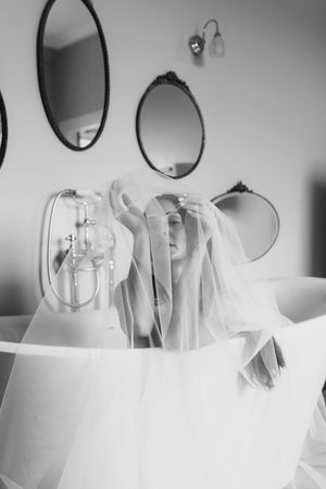 Black and white photo of a freestanding bathtub with flowing tulle fabric and oval mirrors on the wall.