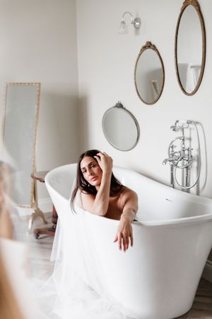 Artistic bathroom photoshoot featuring a classic white clawfoot tub and decorative vintage mirrors on the wall.