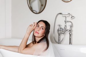 Woman relaxing in modern white bathroom with vintage fixtures and sconce lighting.