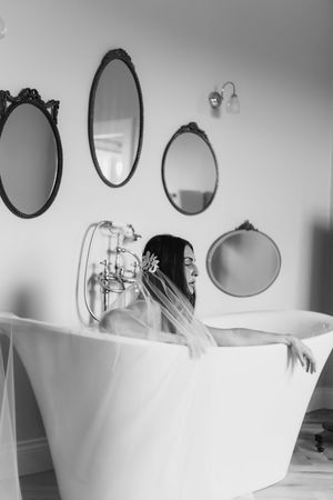 A white freestanding bathtub with vintage-style faucet sits beneath decorative oval mirrors in a serene bathroom setting.