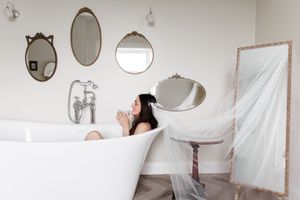 A bright bathroom interior with multiple round mirrors mounted on a white wall and sheer curtains by the window.
