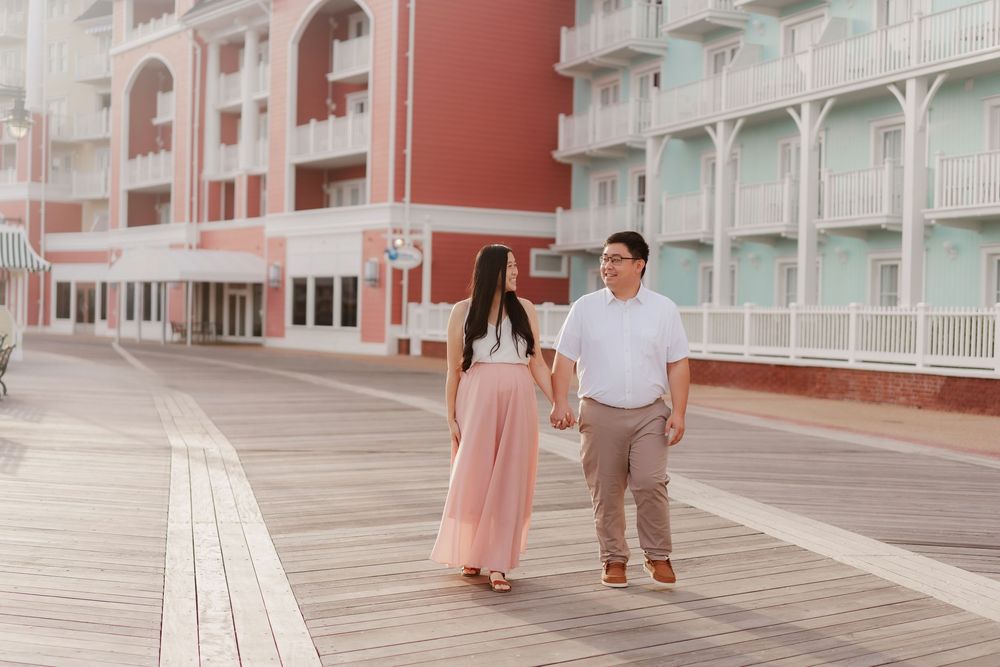 A couple walks hand in hand along a pink-tinted modern architectural corridor with geometric patterns and lighting.