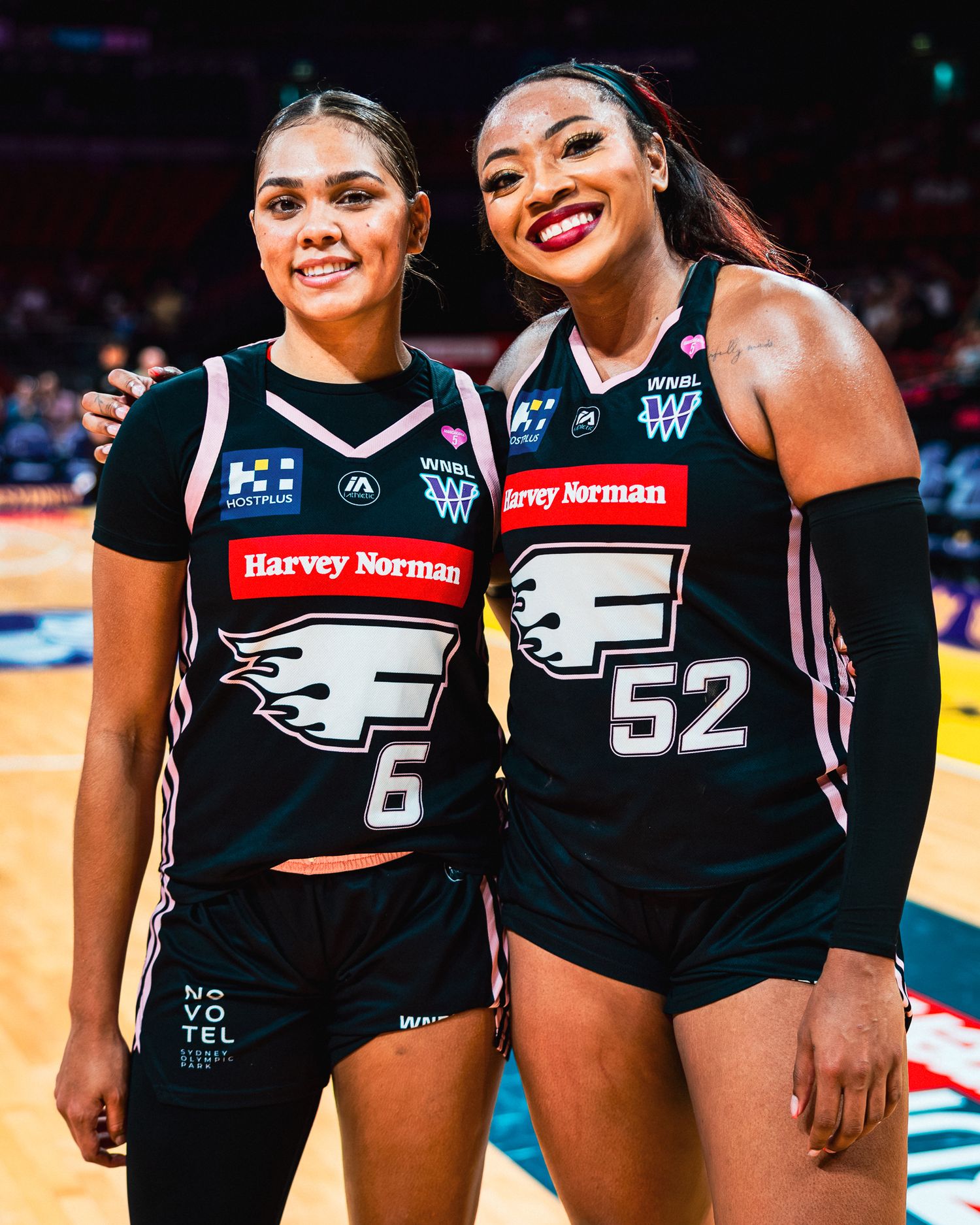 Basketball players in black Harvey Norman uniforms posing together on the court.