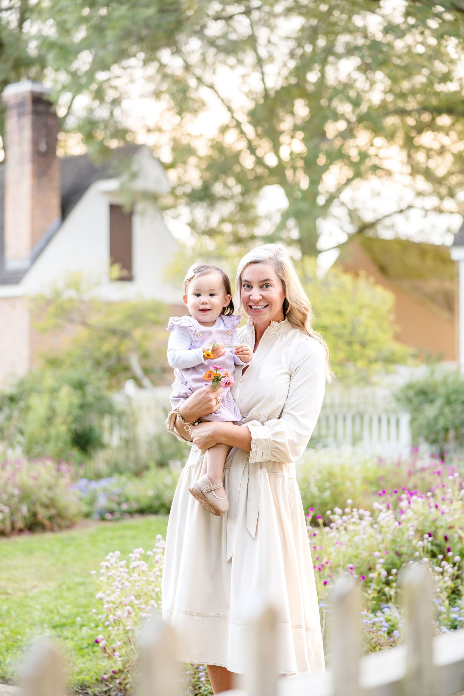 Sample photographer session of a family in Colonial Williamsburg in a blooming flower garden with white picket fences.