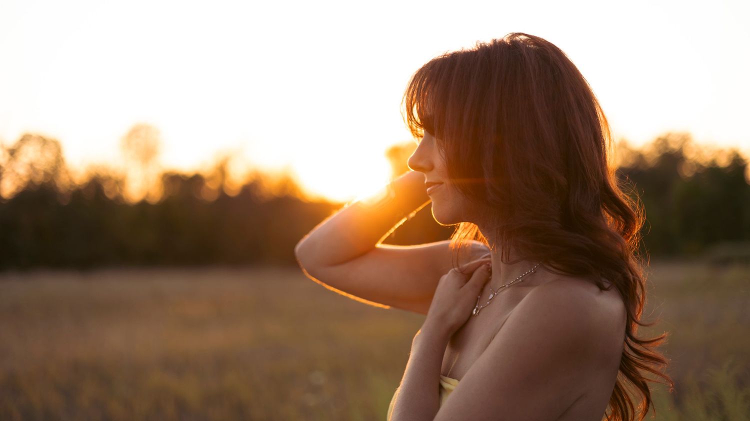 A person stands silhouetted against a golden sunset sky in a field during magic hour.