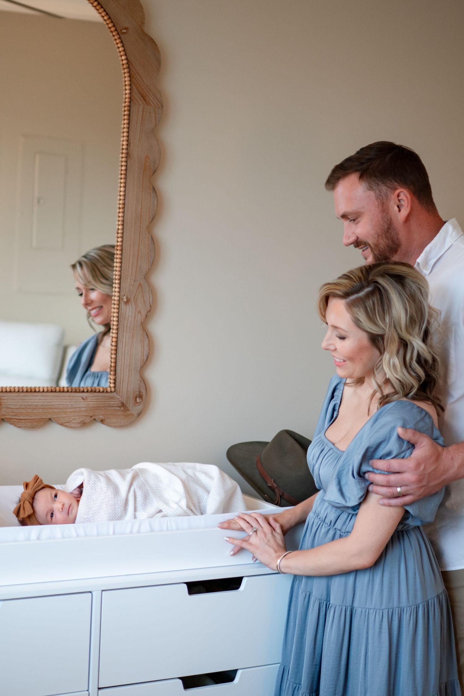 A couple in a blue dress and white shirt lean against a white dresser in a romantic progression of poses.