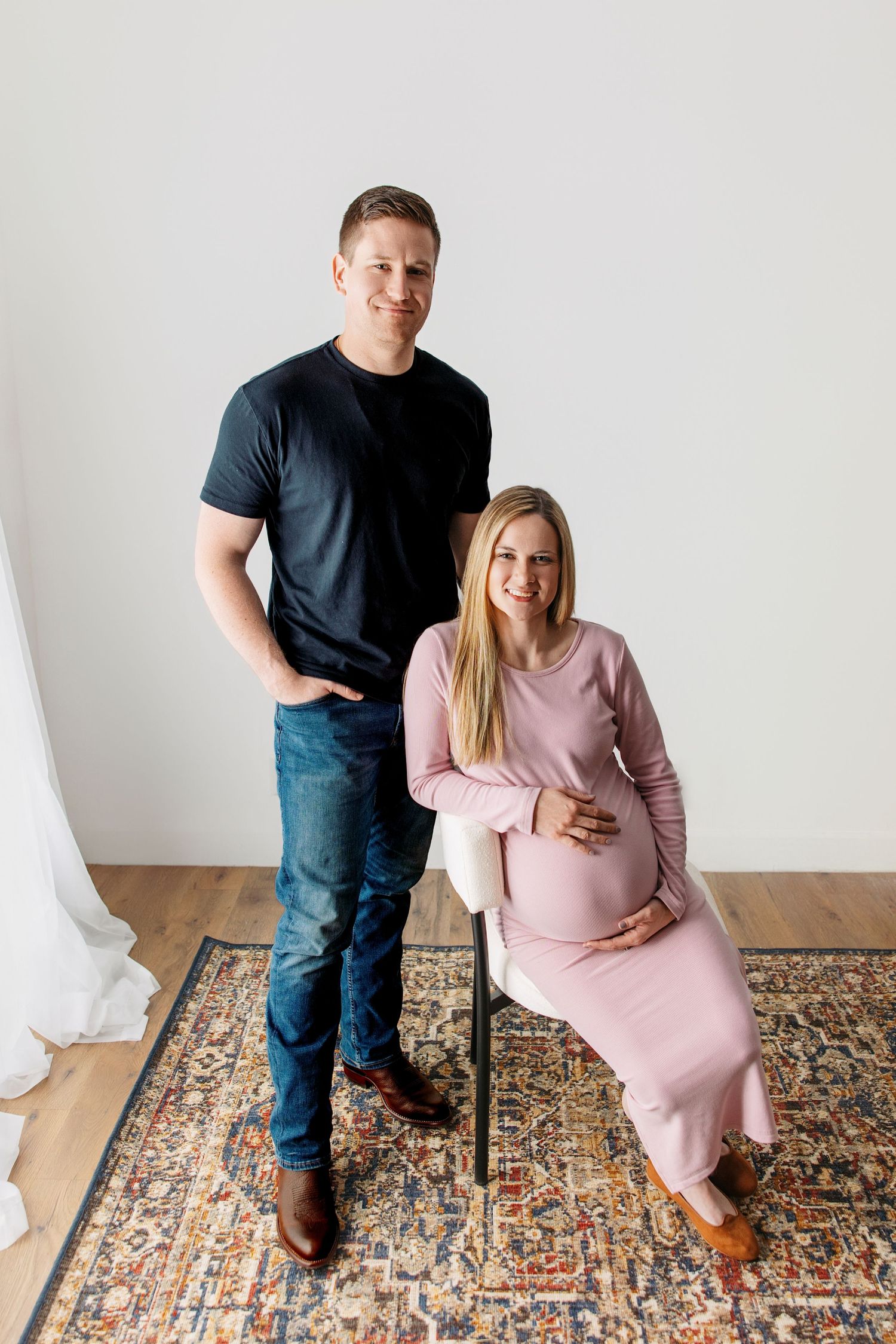 Expectant mom and dad pose together on a patterned area rug in a minimalist room with white walls. Nashville maternity photographer