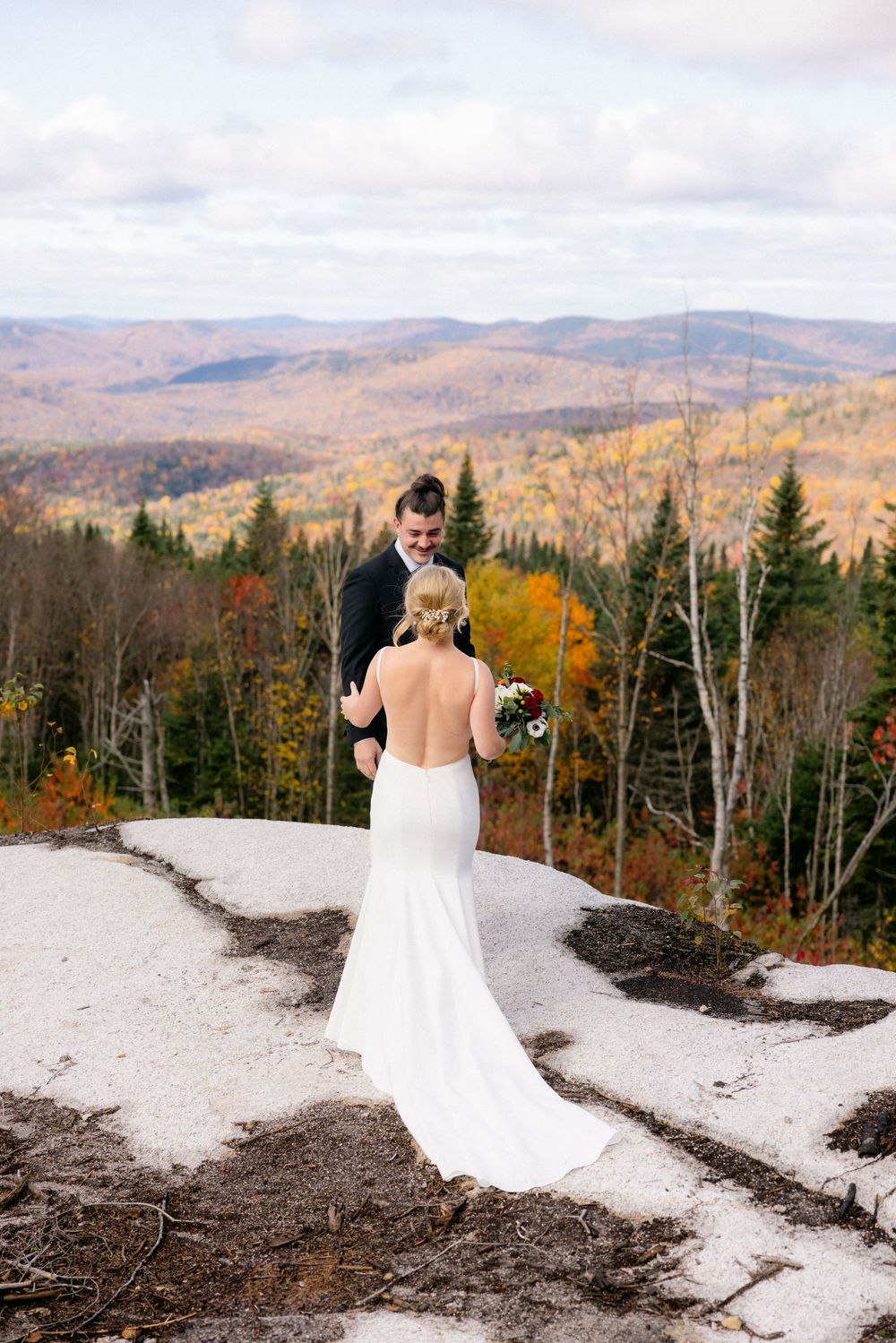 A scenic mountain wedding photo series showing a bride in a white dress against an autumn forest landscape in Vermont.