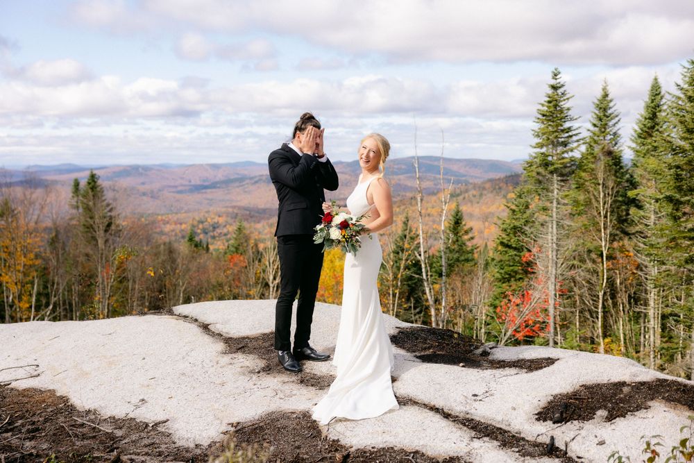 A couple shares an intimate moment on a mountain summit with scenic autumn views of Vermont's landscape in the background.