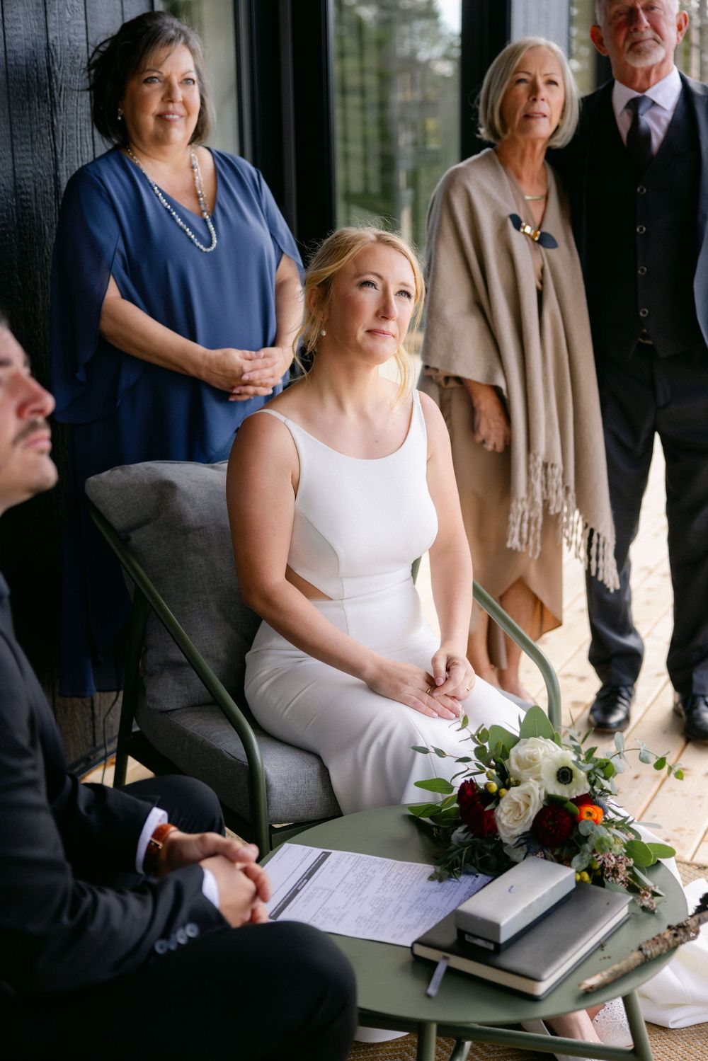 Wedding ceremony document signing scene on a rustic wooden deck with floral bouquet details.