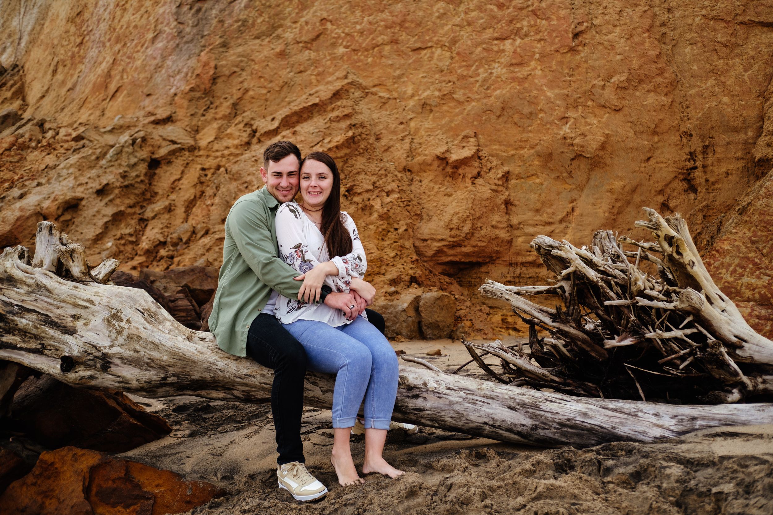 Couple sitting together on a log during a relaxed outdoor photoshoot