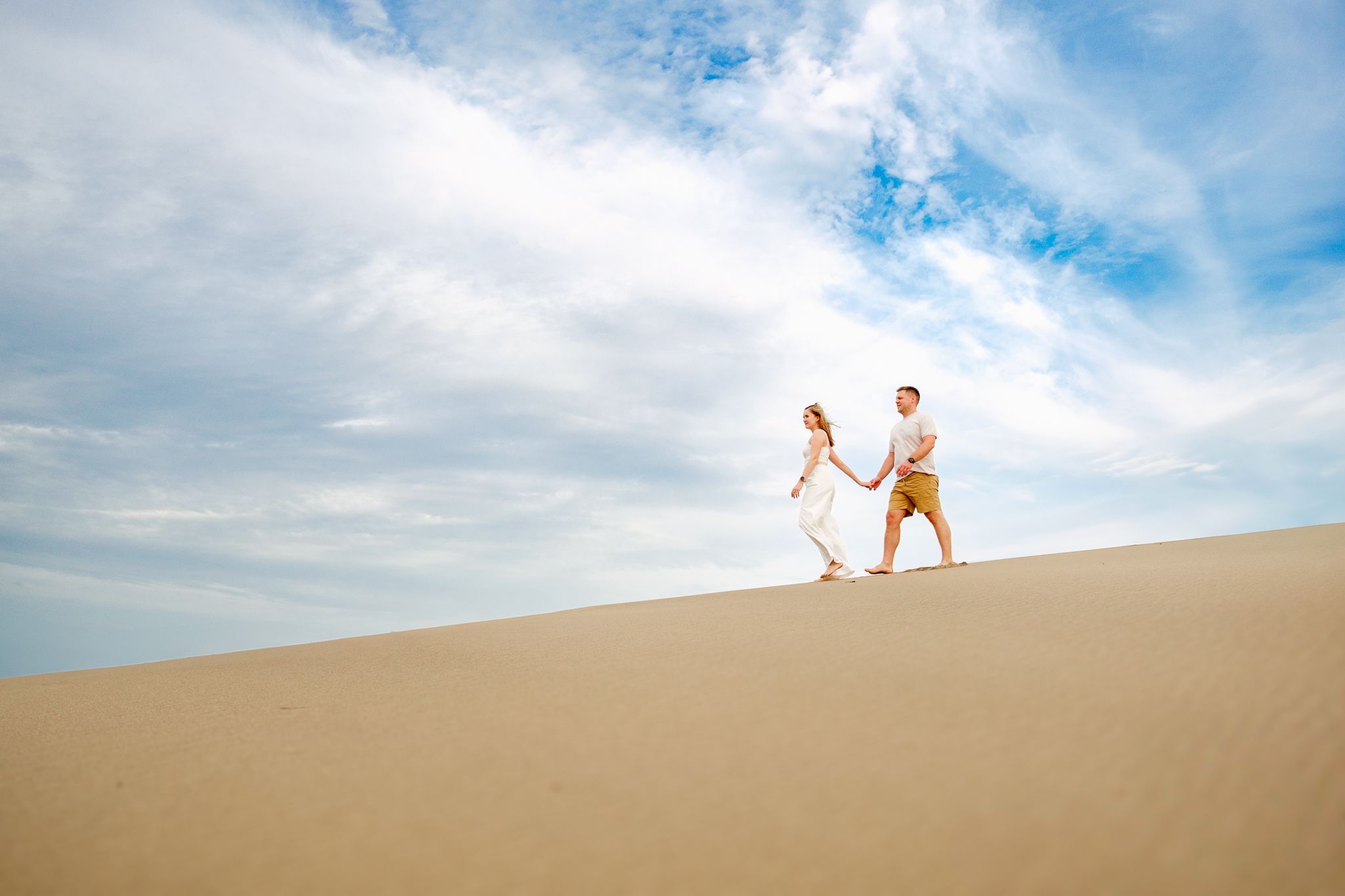 Couple walking along sand dunes at Mtunzini Beach under a dramatic sky