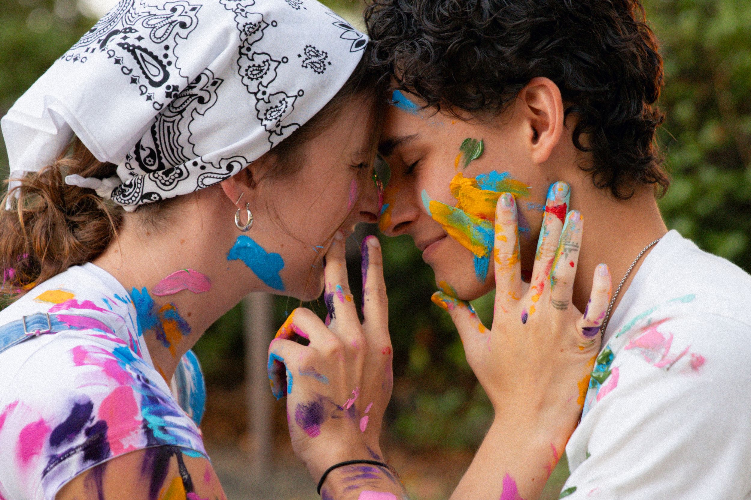 People in colorful tie-dye shirts lean in close together during a group activity outdoors.