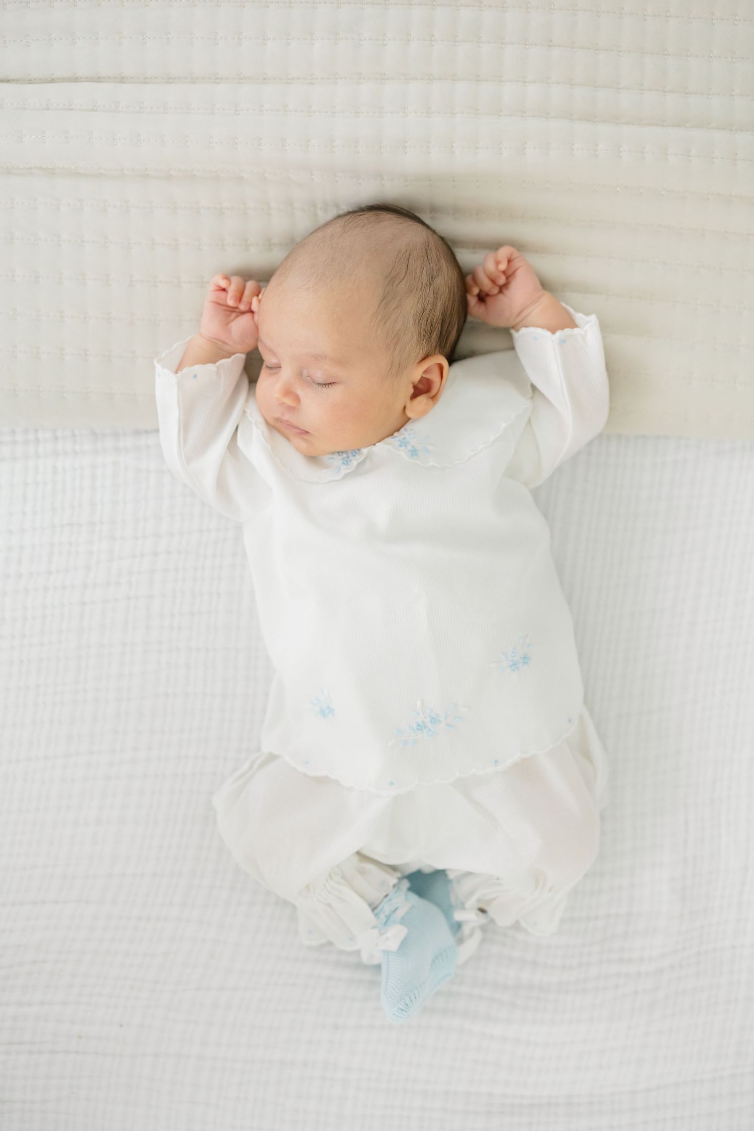 A sleeping newborn baby in white clothing lies on soft white bedding in a series of peaceful poses.