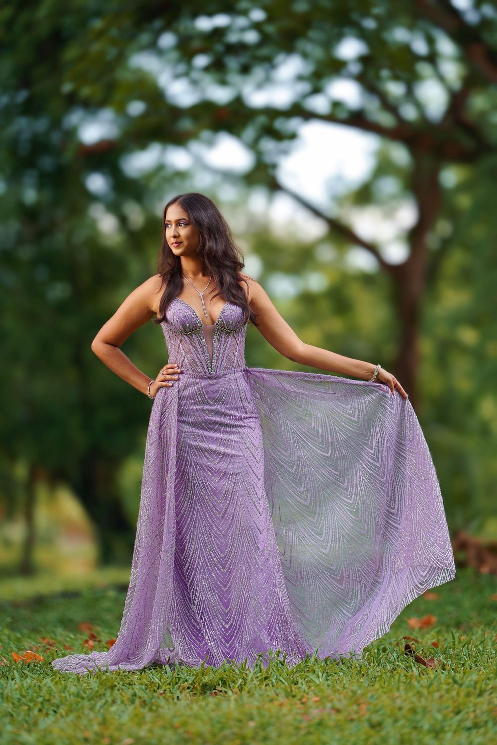 A flowing lavender lace gown is showcased on a grassy hill during a dreamy outdoor photoshoot.