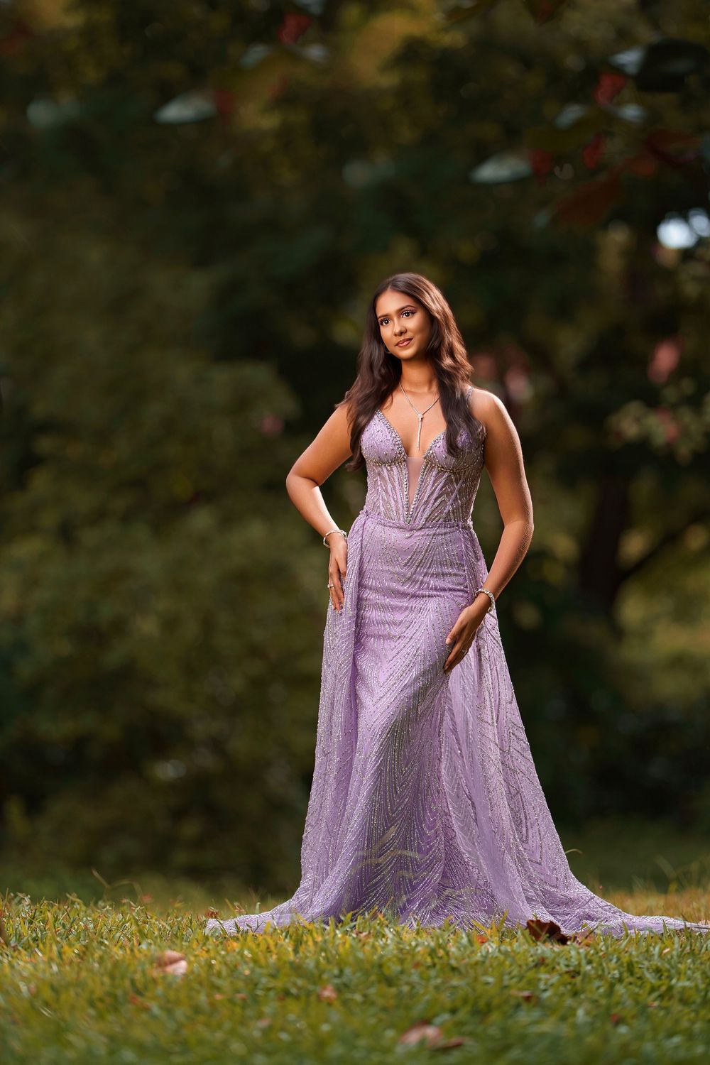 A person in a flowing lavender gown poses gracefully in a grassy outdoor setting during a photo session.