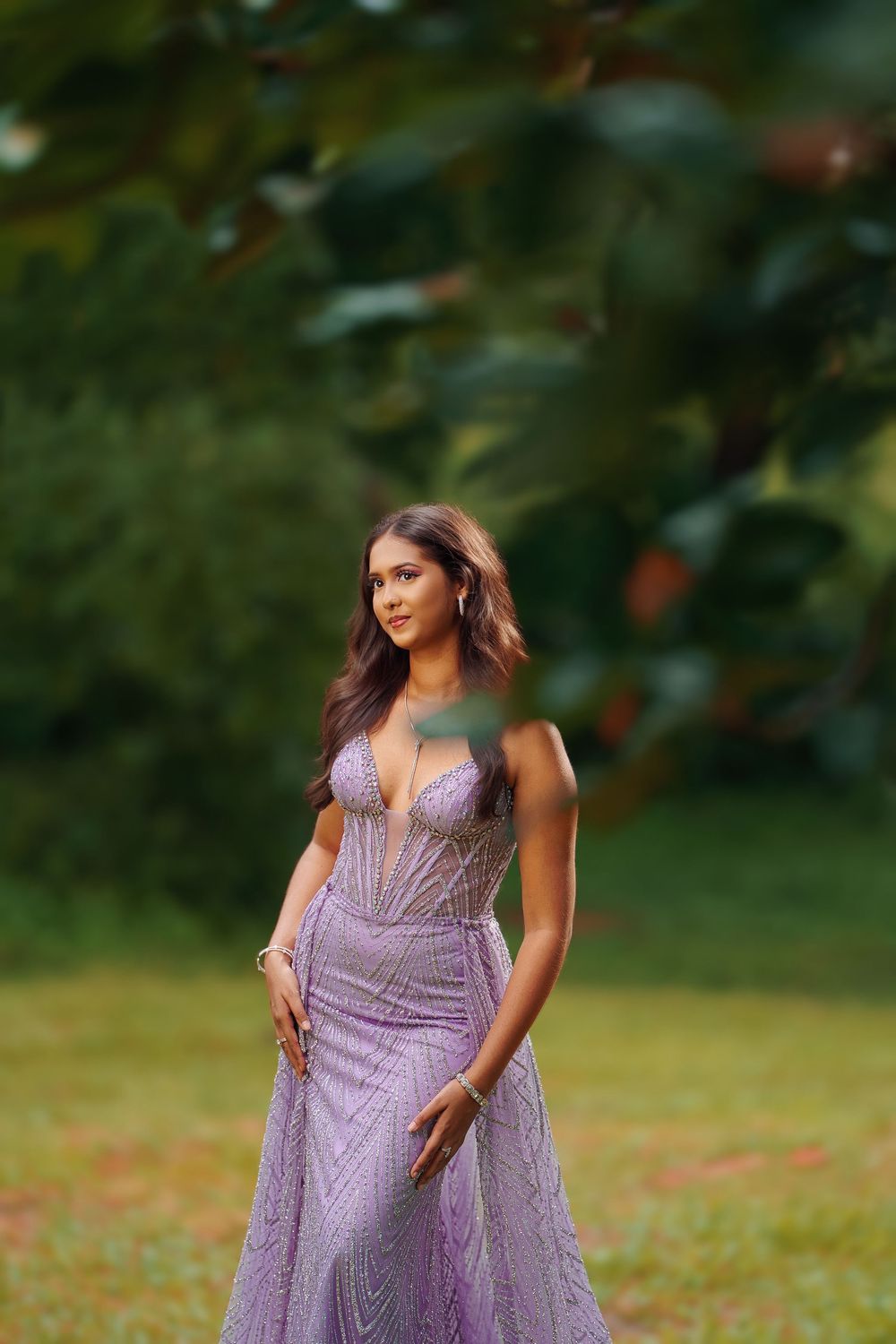 A person in a flowing lavender formal gown poses gracefully in an outdoor garden setting.