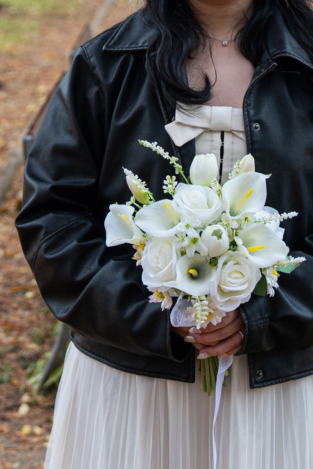 A wedding bouquet of white roses and lilies paired with a black leather jacket against a natural outdoor background.