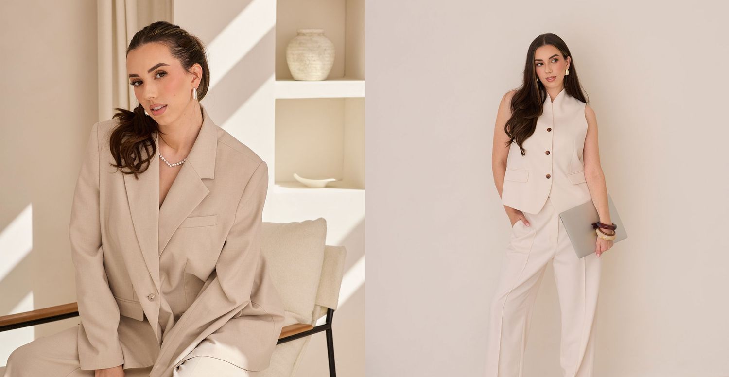 Woman in all-white outfit poses elegantly on beige couch in minimalist setting.