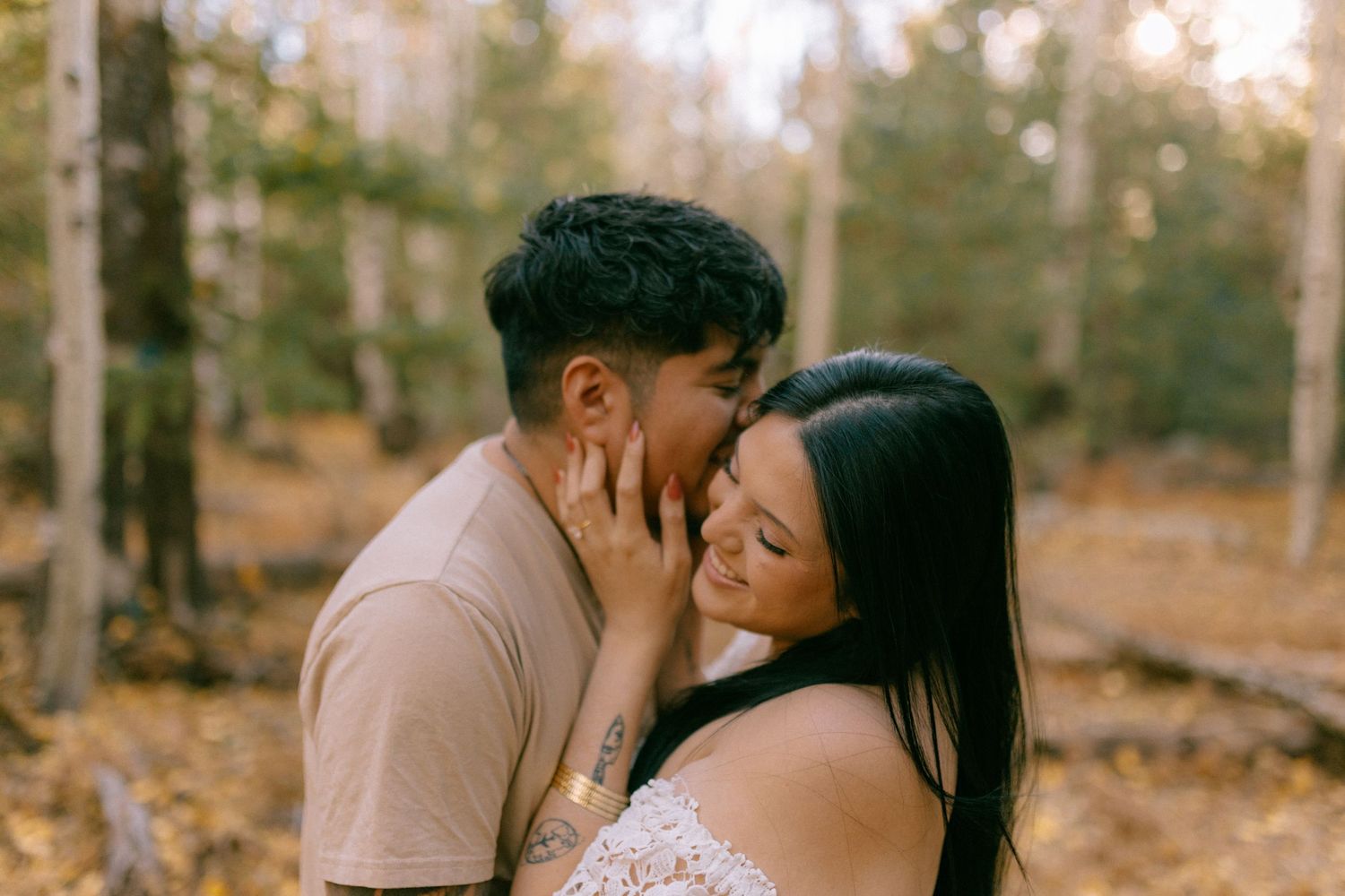 A romantic couple embraces and kisses in an autumn forest setting with golden sunlight filtering through trees.