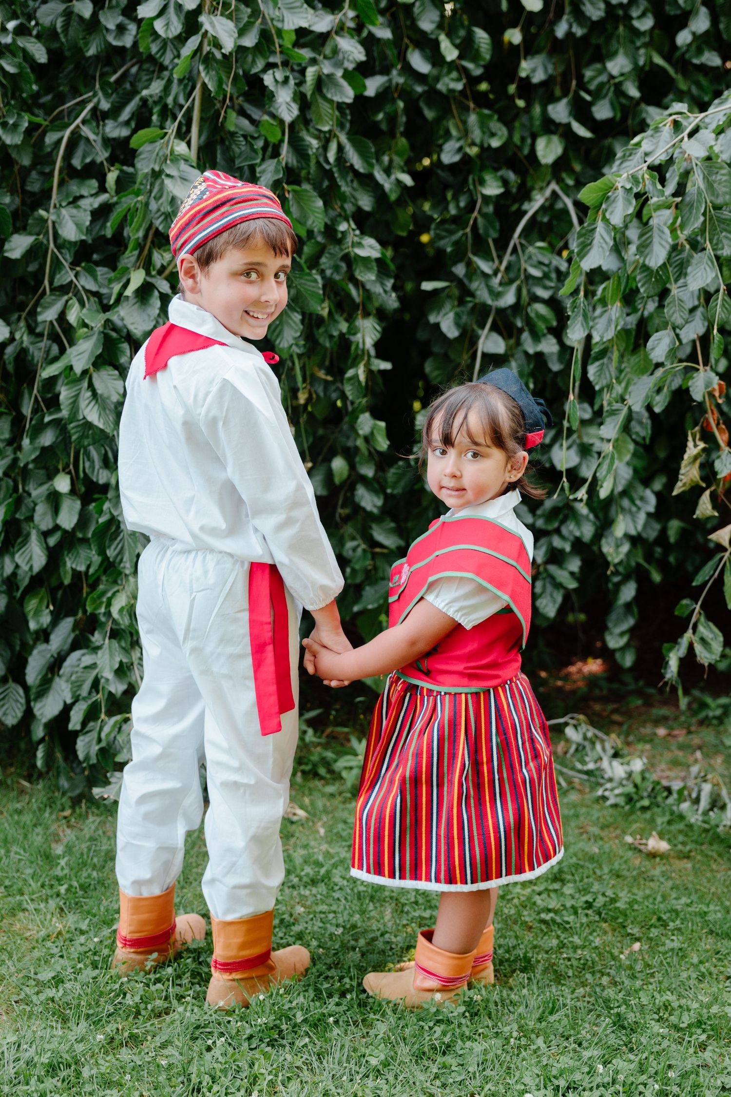 Two children in traditional Estonian folk costumes playing together in a garden setting.