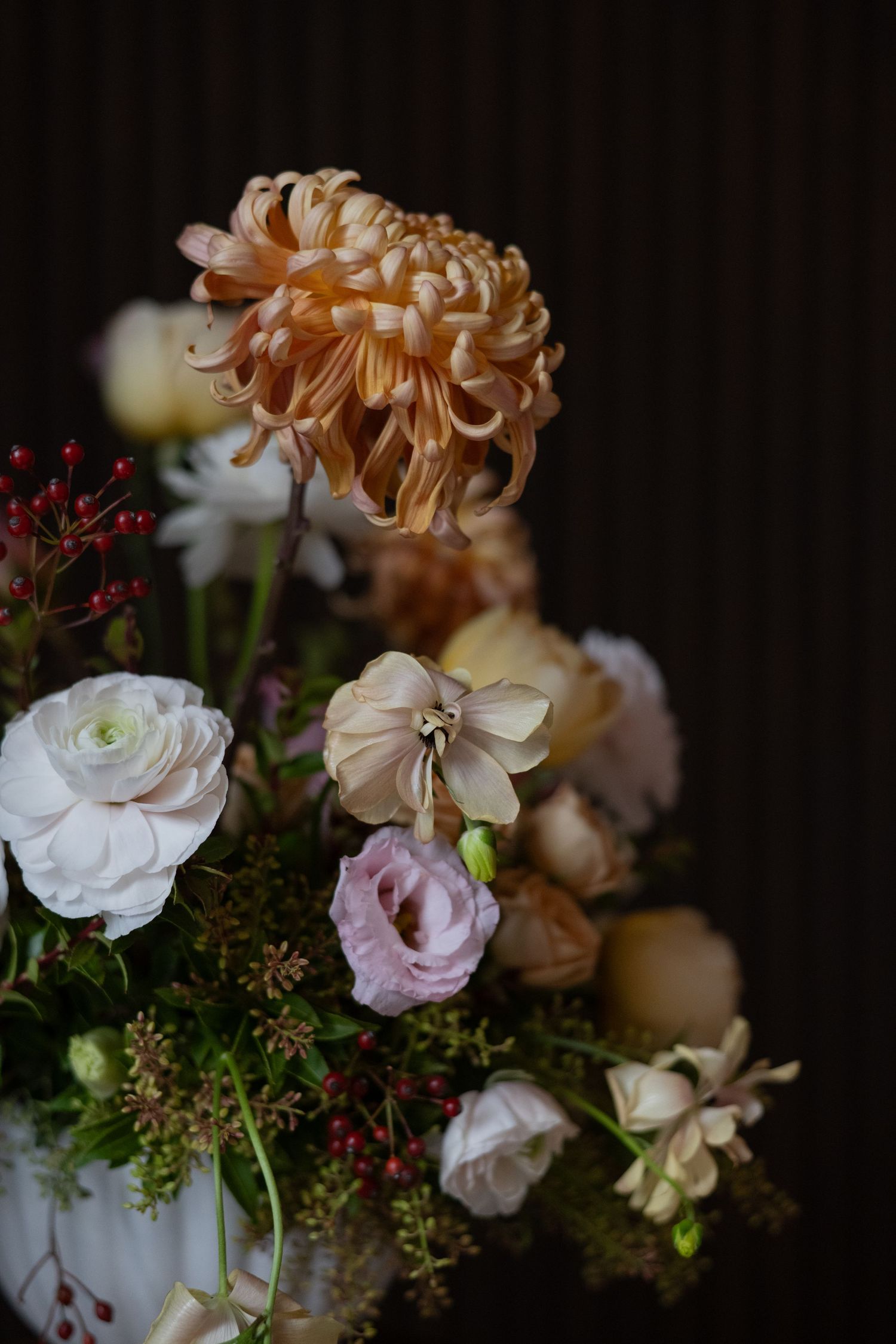 Elegant floral arrangement with white roses and peach chrysanthemums against a dark background.