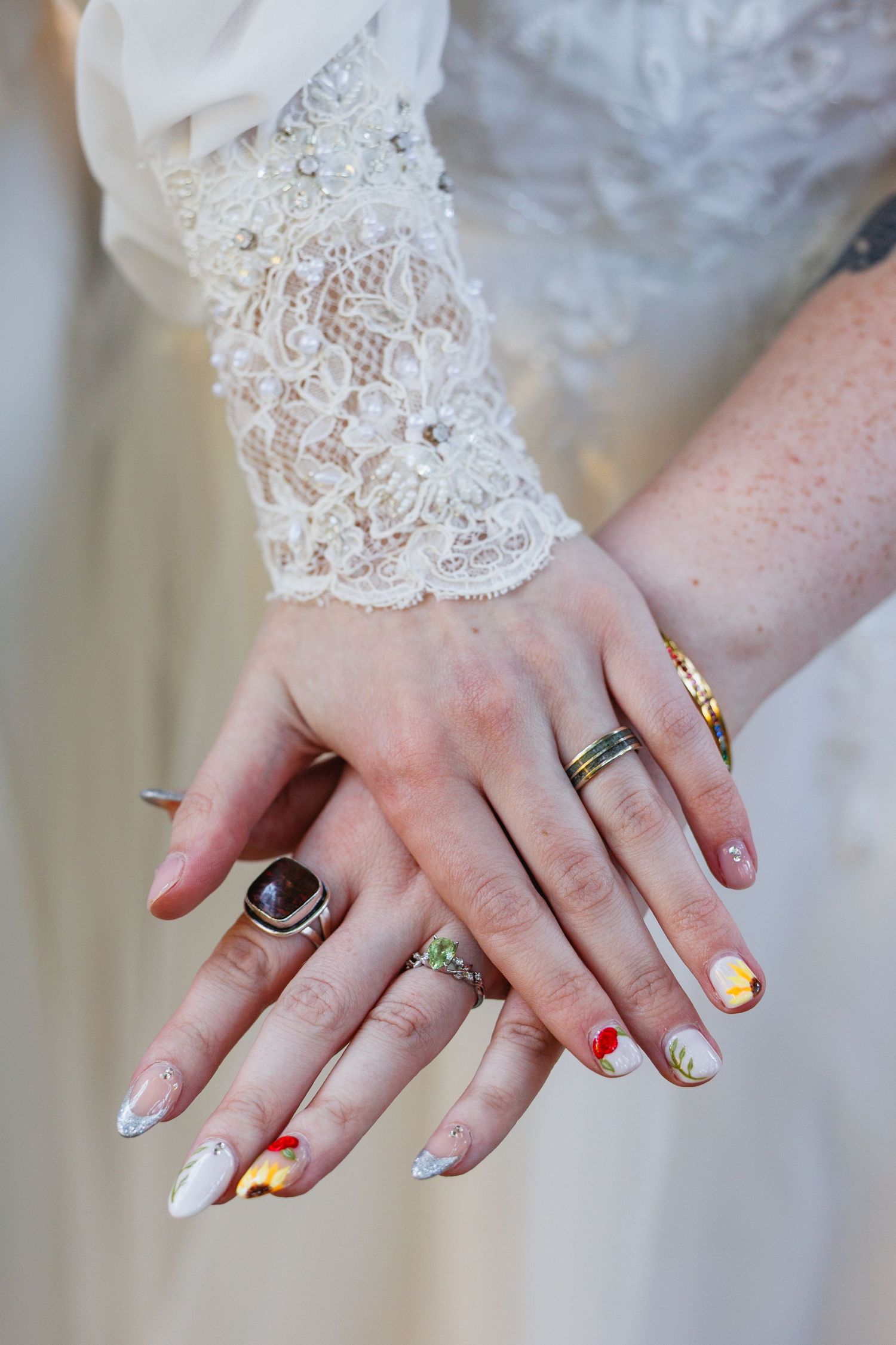 Close-up of bride's hands showing decorative nail art and multiple rings with lace wedding dress sleeve.