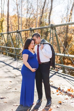 A couple shares a romantic moment on a bridge surrounded by autumn leaves and golden sunlight.