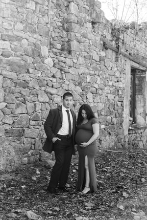 A romantic black and white photo series of a couple posing against a rustic stone wall in formal attire.