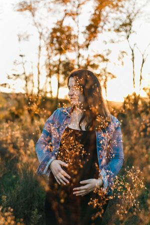 Dreamy sunset portrait with dried flowers floating in golden light through autumn trees in nature.