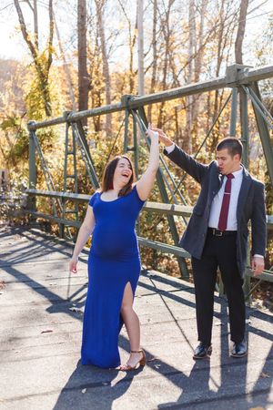 A couple dances playfully on a wooden bridge surrounded by autumn trees.