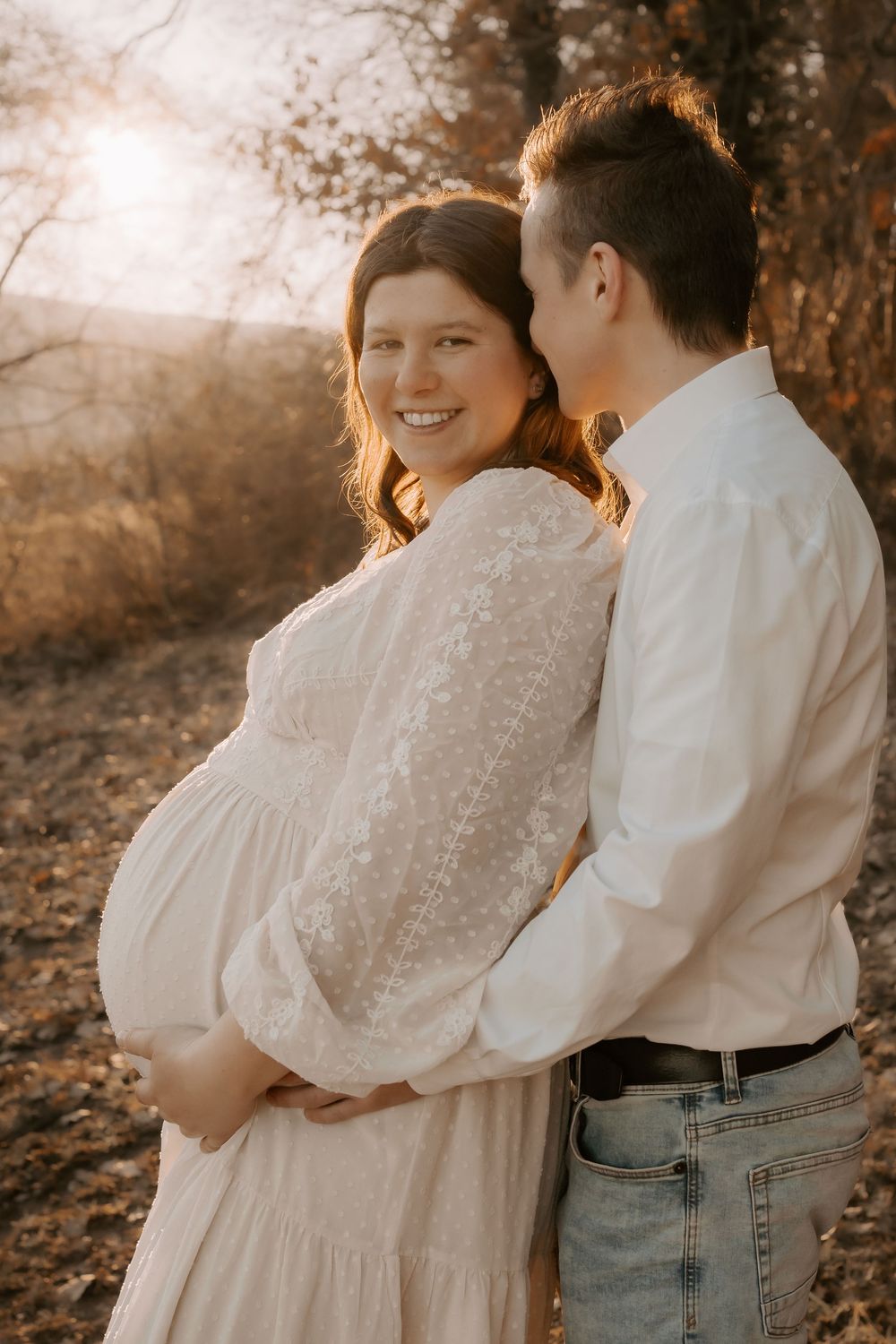 A couple in white and denim embraces outdoors during a romantic sunset photoshoot in autumn.