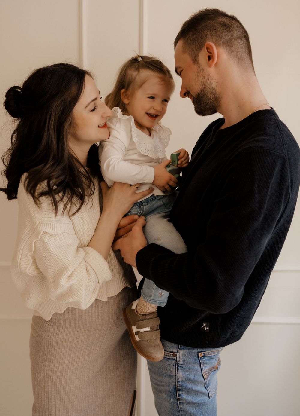A loving family shares tender moments together in a series of candid photographs against a neutral wall.