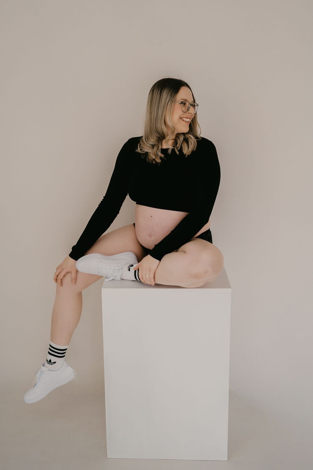 Minimalist photo series showing a person in black top and white socks posing on a white cube against beige background.