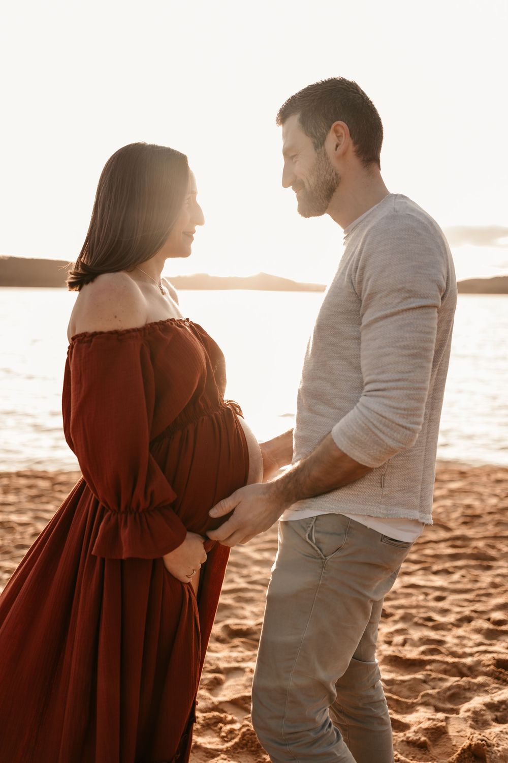 A couple stands together on a sandy beach at sunset in a romantic silhouetted sequence.