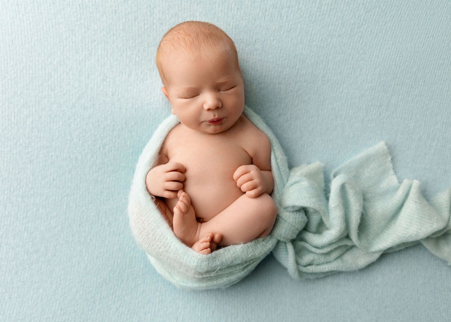 New Hampshire newborn photographer capturing a sleeping baby wrapped in blue, classic studio newborn portrait with gentle tones.