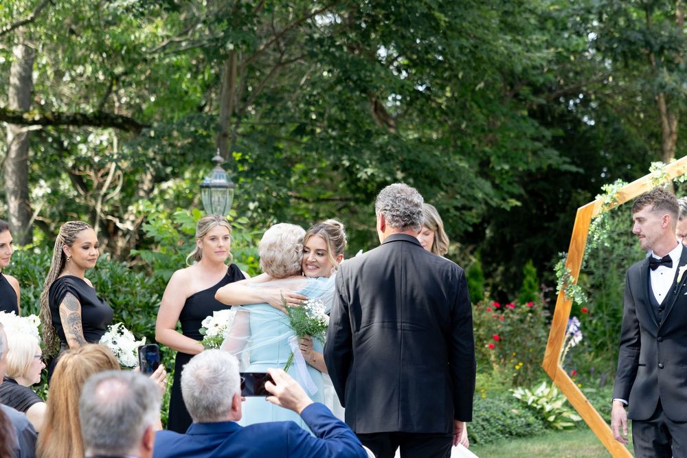 Wedding guests gather outdoors in a garden setting surrounded by lush greenery during a summer ceremony.