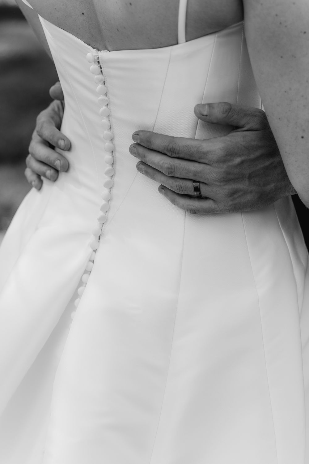 Close-up details of a white wedding dress showing delicate buttons and lace along the back closure.
