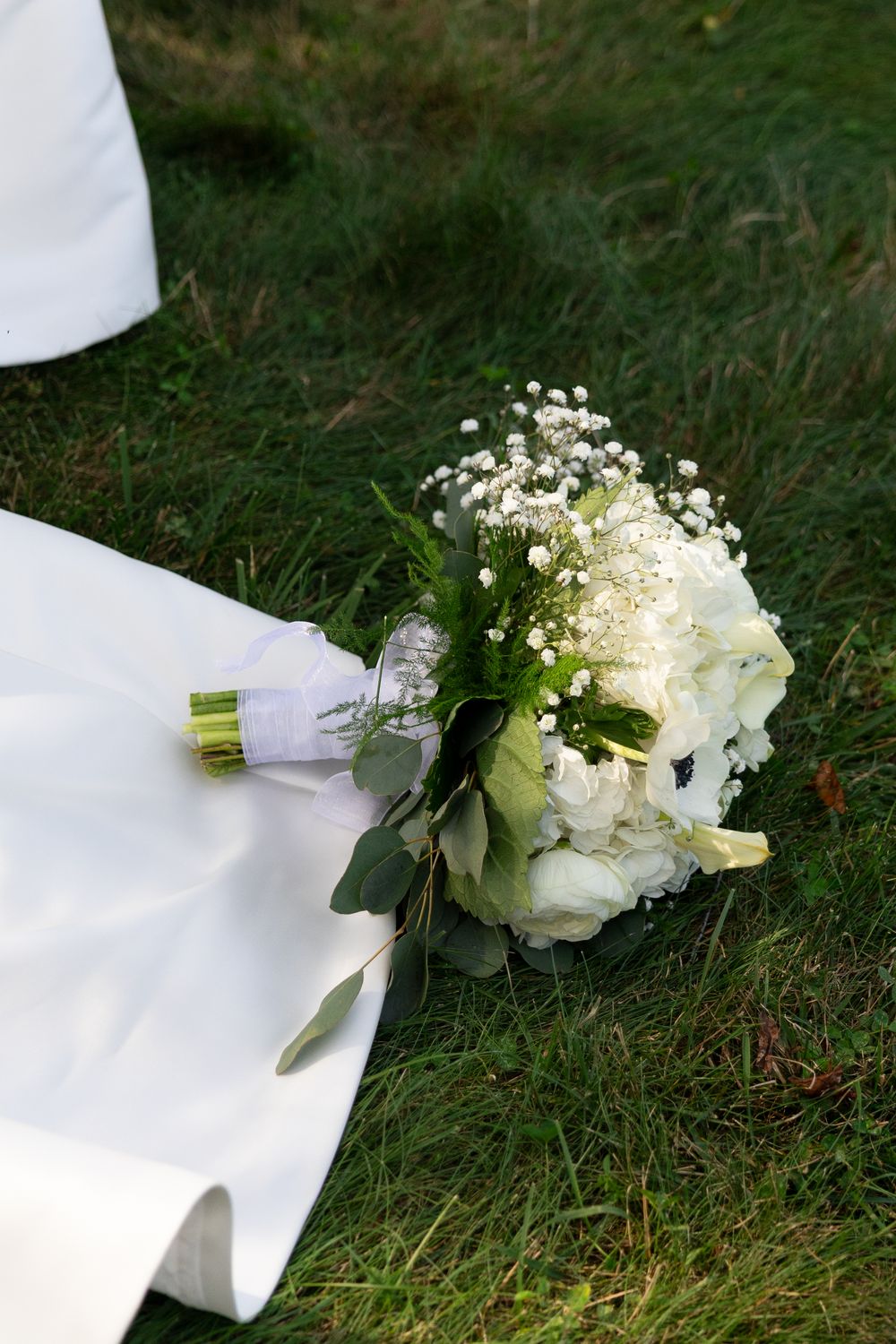 White bridal bouquet with roses and baby's breath lying on grass.