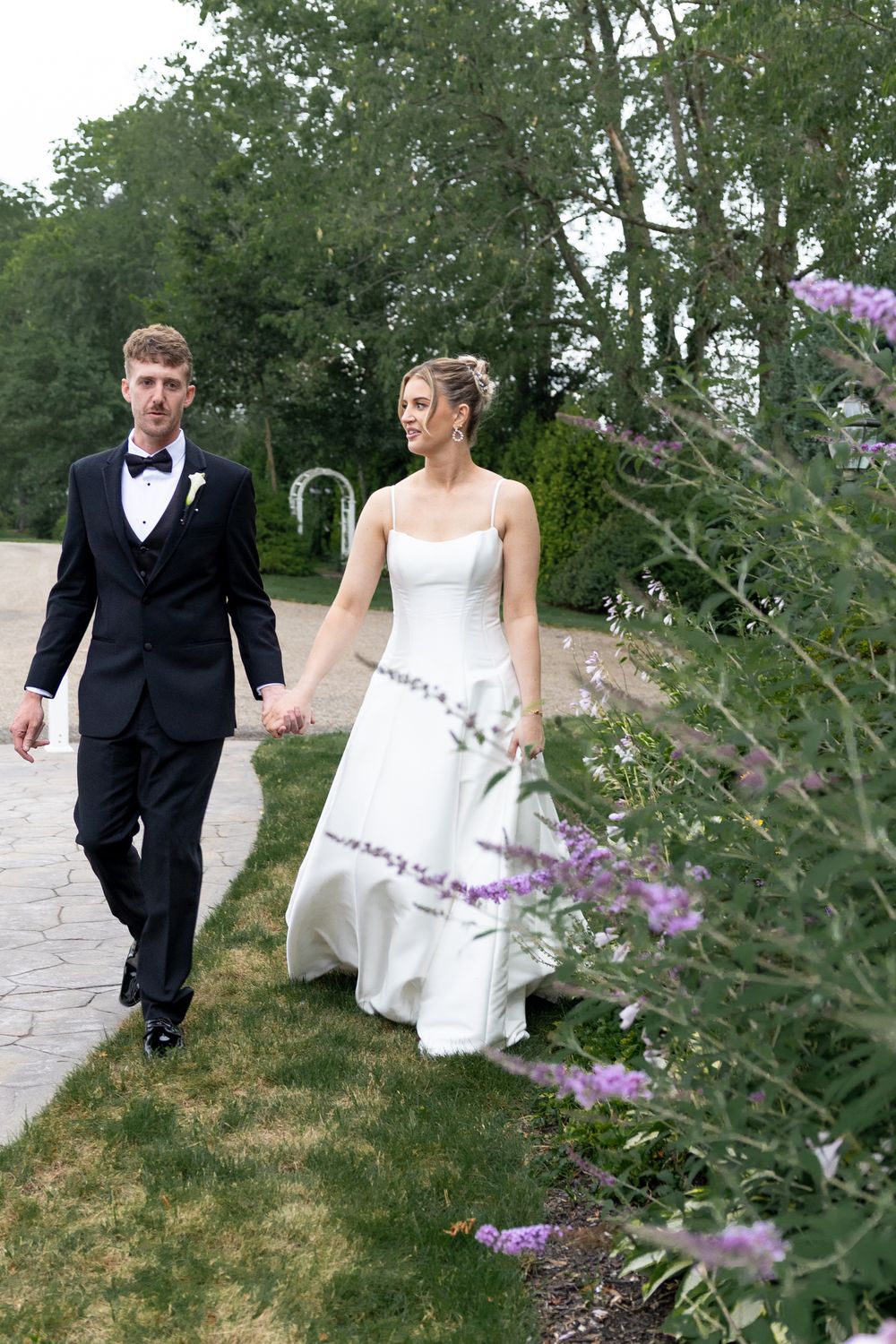Couple walking along outdoor path with purple wildflowers in foreground.